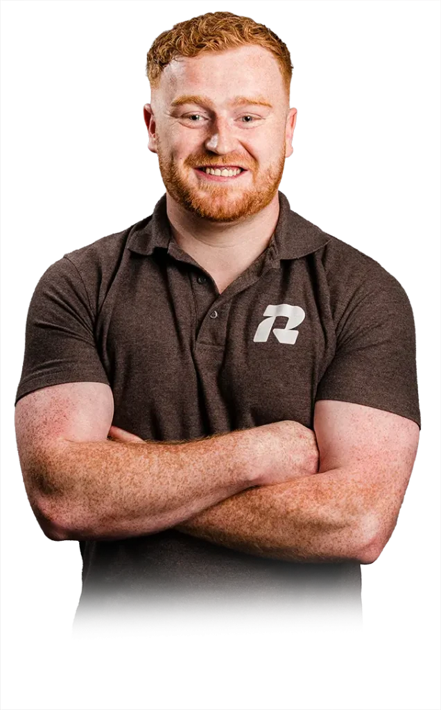Smiling man with red hair and beard, arms crossed, wearing a dark polo with a white logo on the chest.