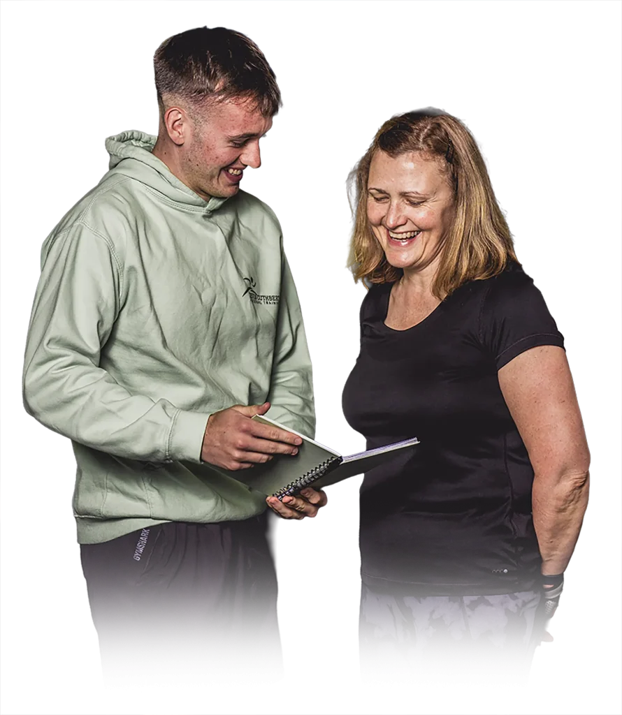 Two people smiling and looking at a spiral notebook together, as if reviewing something.